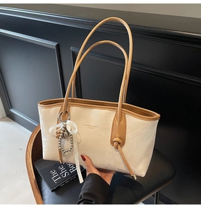 Dettaglio elegante borsa tote beige con finiture in pelle, fiocco e ciondolo di perle