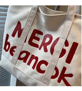 Detailed view of cream canvas tote bag featuring red MERCI beaucoup printed text