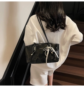 Dettaglio della borsa sottobraccio in pelle nera con nastro bianco e ciondolo di perle