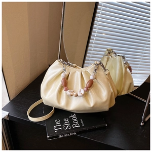 Dettaglio di una borsa a secchiello plissettata beige con manico di perle e riflesso