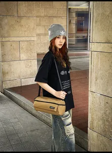 Détail du sac cylindrique kaki avec bandoulière noire et étiquette de marque latérale