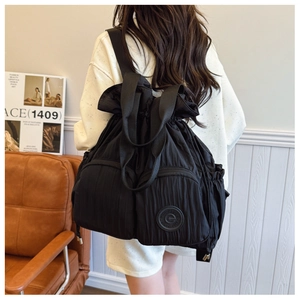 Rear view of a black drawstring backpack with pleated texture worn by a model in a home setting
