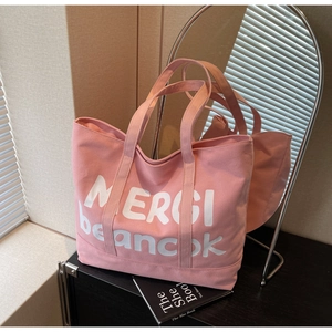 Detail view of pink canvas tote bag with white MERCI lettering and sturdy dual handles
