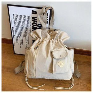 Detail of beige canvas drawstring backpack featuring large pleated opening and front pocket
