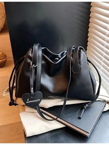 Minimalist black pleated bucket bag with heart pendant on a clean modern background