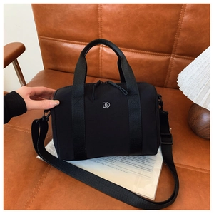 Détail d'un sac Boston en nylon noir avec logo DO en métal sur un canapé en cuir