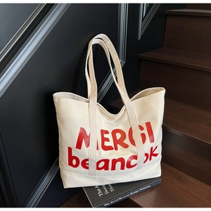 Detailed view of cream canvas tote bag featuring bold red MERCI beancook printed lettering