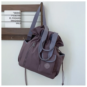 Detail of dark purple pleated bucket bag showing drawstring closure and front zip pocket