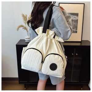 Detail of white drawstring backpack featuring large front zipper pockets and black strap