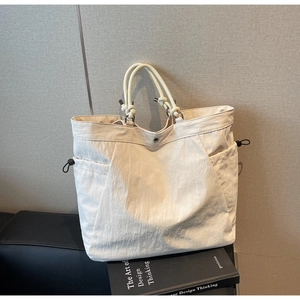 Detail of cream tote bag featuring knotted handles and functional drawstring side pockets