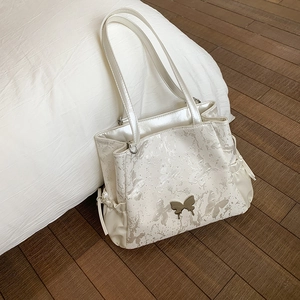 Detail of pearl white tote bag with butterfly prints, metal charm and side drawstring