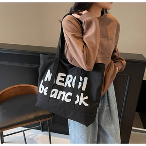 Detail of black canvas tote bag showing white MERCI letter printing and durable handles
