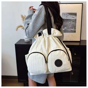Detail of off-white drawstring backpack showing textured fabric and front zip pockets