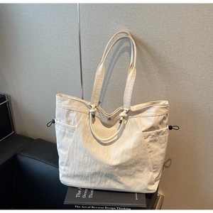 Detail view of large cream canvas tote bag with adjustable side drawstrings and top handles