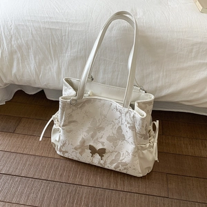 Detail view of cream tote bag featuring butterfly prints and metallic butterfly clasp