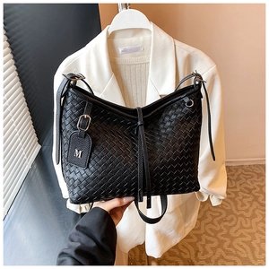 Detailed close-up of black woven shoulder bag with metallic M charm and texture