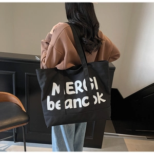 Detail of a large black canvas tote bag with white letter print worn over the shoulder