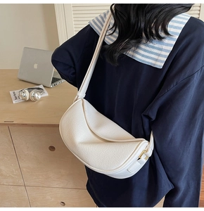 Close-up of white pebble-grain crescent shoulder bag with golden metallic hardware