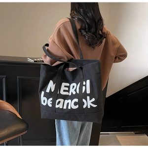 Close-up of black canvas tote bag with white lettering MERCI carried by a model