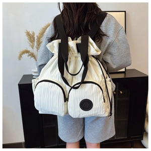 Detail of white pleated backpack featuring drawstring closure and two large zipper pockets