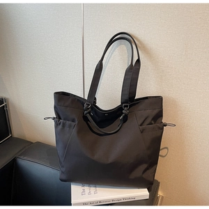 Detail of black nylon tote bag featuring functional drawstring side pockets and wide straps
