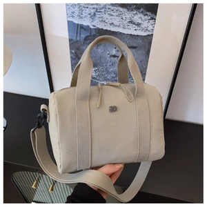 Détail du sac Boston en nylon beige avec poignées tissées et logo métallique central