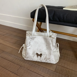Detail of off-white tote bag with butterfly print and elegant metal butterfly charm