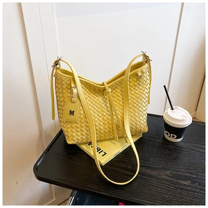 Detail of yellow woven tote bag with slim shoulder straps and M letter pendant charm