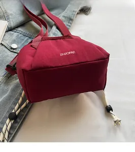 Detail of burgundy nylon bucket bag with drawstring accents and branded embroidery
