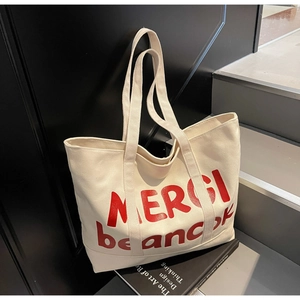 Detail of off-white canvas tote bag featuring red MERCI beaucoup print on dark steps