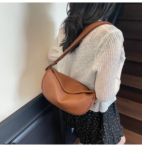 Brown leather crescent shoulder bag shown worn by a model in a minimalist indoor setting