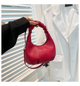 Détail d'un sac à main rouge en cuir grainé avec anse froncée et logo blanc stylé