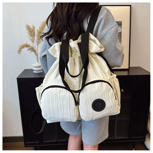 Detail of cream drawstring backpack showing textured fabric and front zip pockets