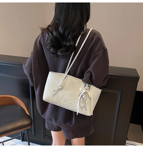 Dettaglio borsa a spalla in pelle bianca con scritta FASHION & BAGS e ciondolo nastro