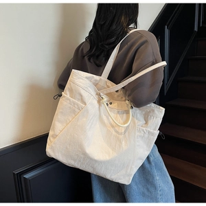 Close-up of a large beige canvas tote bag with side pockets and drawstring details