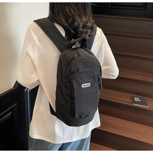 Rear view of a black crinkled nylon backpack with adjustable straps on a wooden staircase