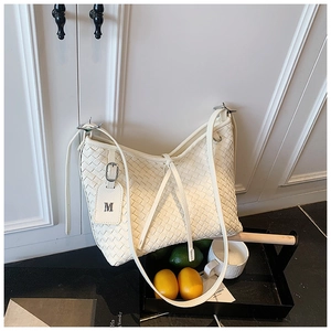 Detail of white woven faux leather tote bag with a metallic M-letter charm decoration