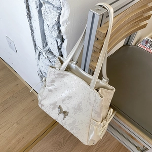 Detailed view of beige tote bag with butterfly print and metal buckle on wooden chair