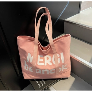Detail of pink canvas tote bag with white MERCI beaucoup lettering and sturdy handles
