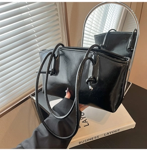 Détail du sac cabas noir brillant avec de longues anses nouées dans un cadre moderne