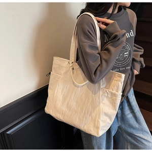 Detail of a large off-white nylon tote bag with side drawstring pockets shown on model