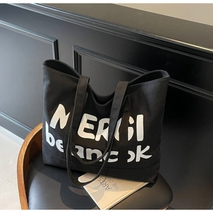 Detailed view of black canvas tote bag with white letter print on a stylish chair