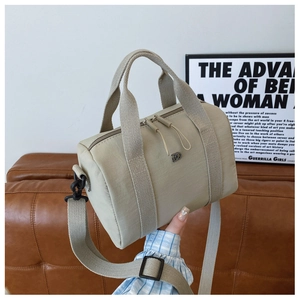 Gros plan du sac bowling en nylon beige avec logo métallique et bandoulière réglable
