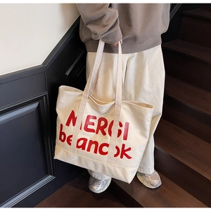 Detail of cream canvas tote bag featuring red MERCI letter print and textured shoulder strap