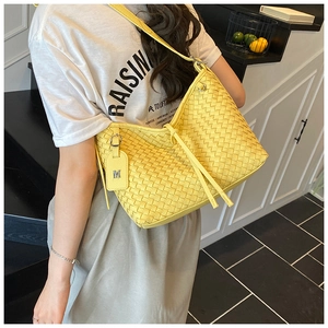 Detail of yellow woven leather tote bag with metallic letter charm on a shoulder strap