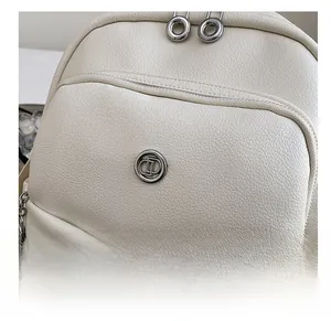 Detail of off-white lychee leather texture with silver zipper and metallic logo emblem