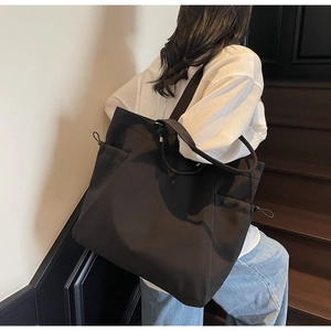 Detail of black canvas tote bag showing side drawstring pocket and durable strap