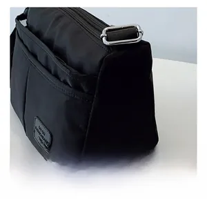 Detail of multi-pocket black nylon shoulder bag showing silver buckles and zipper layers