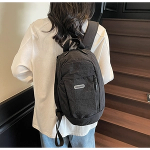 Detail of black wrinkled nylon backpack with brand patch on vintage wood stairs