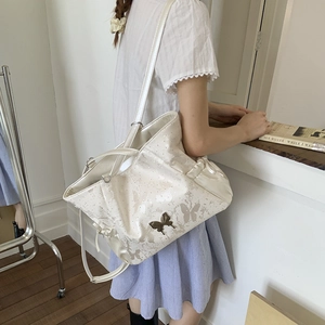 Detail showing the cream tote bag with butterfly prints and metal bow clasp on a model